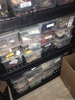 Multiple plastic storage bins stacked on shelving filled with various electronic parts and hardware.