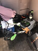 Full view of snow blower inside shed showing wheels, discharge chute, handle, battery and debris on floor