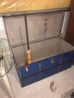 Blue steamer trunk open showing interior lined with mesh-pattern material, metal reinforcements, and visible wooden stand part inside