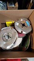 Box containing multiple spools of wire including metal and cardboard spools