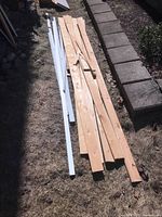 Overview of assorted wooden planks and white metal shelving rods outdoors on grass next to a sidewalk.