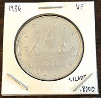 Obverse of the 1936 Canadian silver dollar coin showing the voyageur and Indigenous person canoe scene with 'CANADA DOLLAR 1936' inscriptions and silver content noted on holder