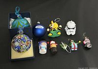 Lot of 10 assorted Christmas ornaments including glass balls, character figures, and themed decorations arranged on a black background.