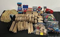 Large collection of wooden train pieces, plastic accessories, mountain tunnel and buildings arranged on table