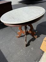 Full view of antique coffee table showing white marble oval top and wooden base with carved legs.