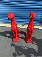 Photo of two bright red ceramic dog statues standing on a pavement with a blue background wall.