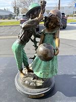 Full view of bronze statue featuring boy raising ball and girl holding ball, with green patina and detailed attire.