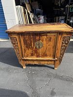 Front view of the Chinese wooden cabinet showing hand carved floral motifs and round metal latch on doors.