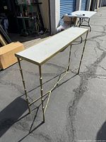 Full view of narrow table with white marble top and bronze bamboo-style legs on outdoor pavement