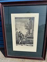 Photo of framed lithograph showing Mozart at a keyboard instrument with two other figures in classical outdoor setting.