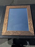 Front view showing rectangular mirror with mosaic style textured frame in a copper or bronze tone.