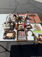 Wide shot displaying the arrangement of all native Indian dolls, books, necklaces, and other themed items on a white table outdoors.