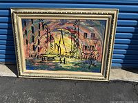 Photo of a large framed oil painting depicting a colorful cityscape with buildings, bodies of water, boats, and people under a vibrant sky.