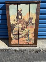 Front view of a painting on wooden panels showing a cowboy on horseback.