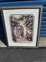 Framed photo print depicting a stone arch with flowering plants and garden scene, in a silver-colored frame with matting.