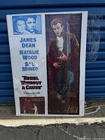 Poster showing James Dean in a leather jacket standing next to a brick wall with inset images and movie credits on the left side.