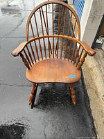 Front view of 19th century wooden rocking chair with curved spindle back and contoured seat on wet ground.