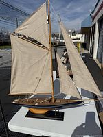 Front and side profile photo showing full model sailboat with beige sails on black base