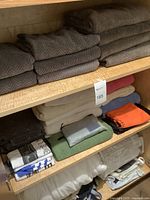 Various folded blankets and comforters in beige, blue, orange, green, white, and tote bags on shelves