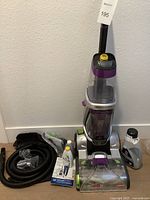 Full view of the Bissell upright carpet cleaner with hose, cleaning chemicals, other accessories arranged around it on floor.