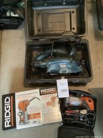 Black & Decker Wood Hawk circular saw in black plastic case, alongside Ridgid compact router in carrying case with original packaging box visible
