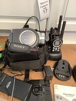 Sony DVD Handycam camcorder in carrying case alongside power adapter and assorted cords, also shows Motorola Talkabout two-way radios on charging dock with user manual