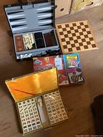 Overview photo showing Mahjong set open with tiles, Monopoly Electronic Banking box, Backgammon set open with dice and pieces, and wooden Chess board.