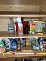 Shelf with ammonia, CVS Health alcohol, leather cleaner, Swiffer dusters, and a red bucket along with several cleaning tools.