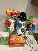 Assortment of cleaning and laundry supplies on a counter including stain removers, detergents, boxes, lint roller, and small plush toy