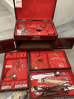 The jewelry box full of assorted costume jewelry pieces, some compartments open, showing multiple jewelry items including rings, bracelets, and necklaces.