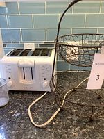 White Cuisinart 4-slice toaster shown with settings and controls visible, placed on countertop with metal two-tier fruit basket beside it