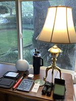 Overview photo of all items on a wooden table near window showing binocs, diffuser, lamp, tumbler, Kindles, selfie stick.