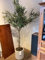 Full view of the faux olive tree in the white planter against a wall, showing tree height and density of foliage.