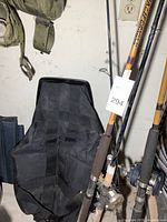 Black nylon rolling bag standing upright with fishing rods leaning against it and green canteen strap visible overhead