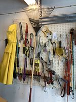 Wide view of pegboard with gardening tools, hand tools, measuring and cleaning tools hanging, and a yellow raincoat on the left