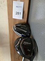 Two driver heads mounted on wood panel showing TaylorMade SIM Max and Titleist 917D2