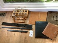 Wide view of lot showing samurai swords with cases, glass propagation vases in wooden stands, and various binders and document cases on wood floor.