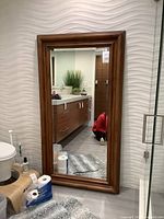 Full view of mirror leaning against textured wall in a room, showing brown wooden frame and reflective surface