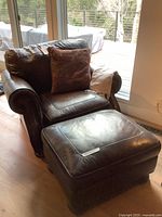 Brown leather armchair and matching ottoman positioned in front of a sliding glass door, showing front and side views with pillow and throw blanket.