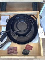 Three cast iron Lodge skillets stacked inside a drawer with cleaning and handle accessories visible
