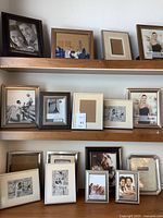 Overall view of multiple picture frames arranged on shelves showing mixed sizes and finishes including wood and metal frames