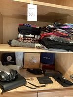 Shelf showing Bose folding headphones on a black cushion, wooden Ashton cigar box, multiple empty watch boxes, luggage tags, and folded scarves stacked.