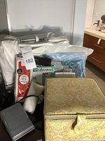 Singer sewing machine in white carrying case, sewing kit with yellow floral box, heat bond adhesive, and various sewing supplies