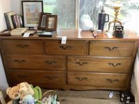 Front view of the Thomasville Impressions wooden dresser with items displayed on top and three drawers open.