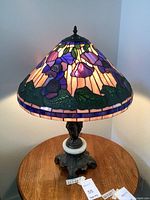 Full view of lamp with floral purple and pink mosaic stained glass shade lit, on wooden table.