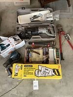 Overview photo showing multiple tools laid out on the floor, including a Porter Cable saw in case, Stanley miter box, bolt cutter, Black & Decker sander, wrenches, sanding tools, and sandpaper.