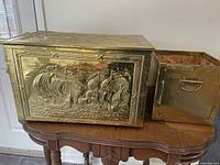 Large brass box with hinged lid and detailed embossed sailing ship pattern on the front, sides, and top, showing texture and craftsmanship.