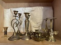 Overview of all 9 brass items including 4 pairs of candlestick holders, one single holder, and candle snuffer arranged on a shelf.