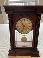 Front view of Bulova mantel clock showing pendulum, wooden frame with mahogany stain, and carved columns.