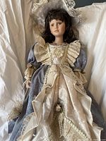 Full body shot showing the porcelain china doll dressed in Victorian-style gown, standing on white fabric background.